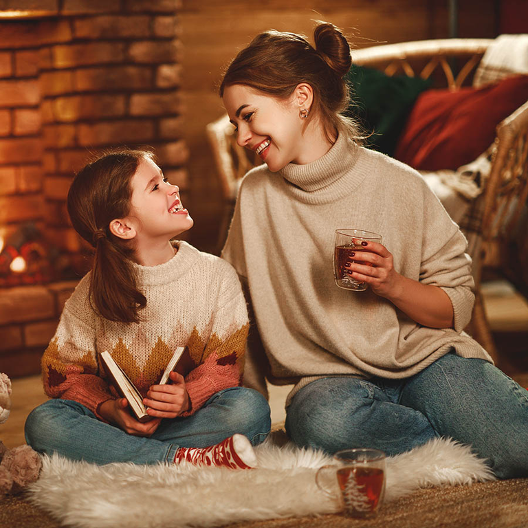 family mother and child reading book and drink tea on winter evening by fireplace